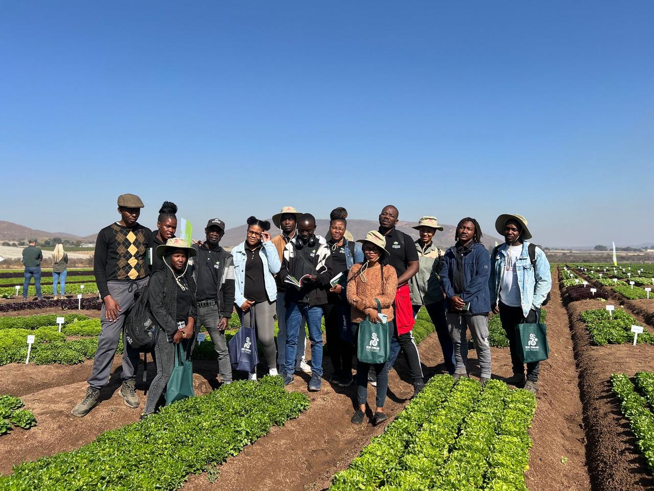 A group of trainees standing between rows of crops in an open field